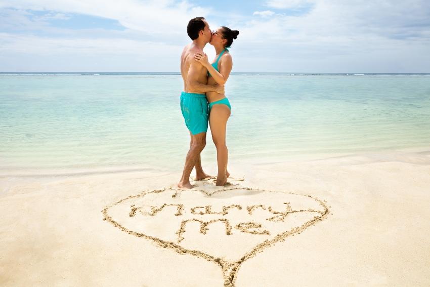Paar en geschilderd hart "Marry me" in het zand